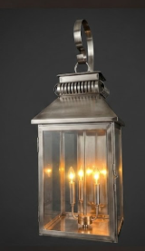 Decorative outdoor lantern with three lights attached to a stone wall.