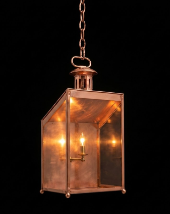 Vintage-style brass hanging pendant light lantern with a light bulb inside on a black background