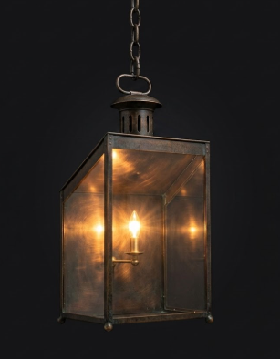 Vintage-style brass hanging pendant light lantern with a light bulb inside on a black background