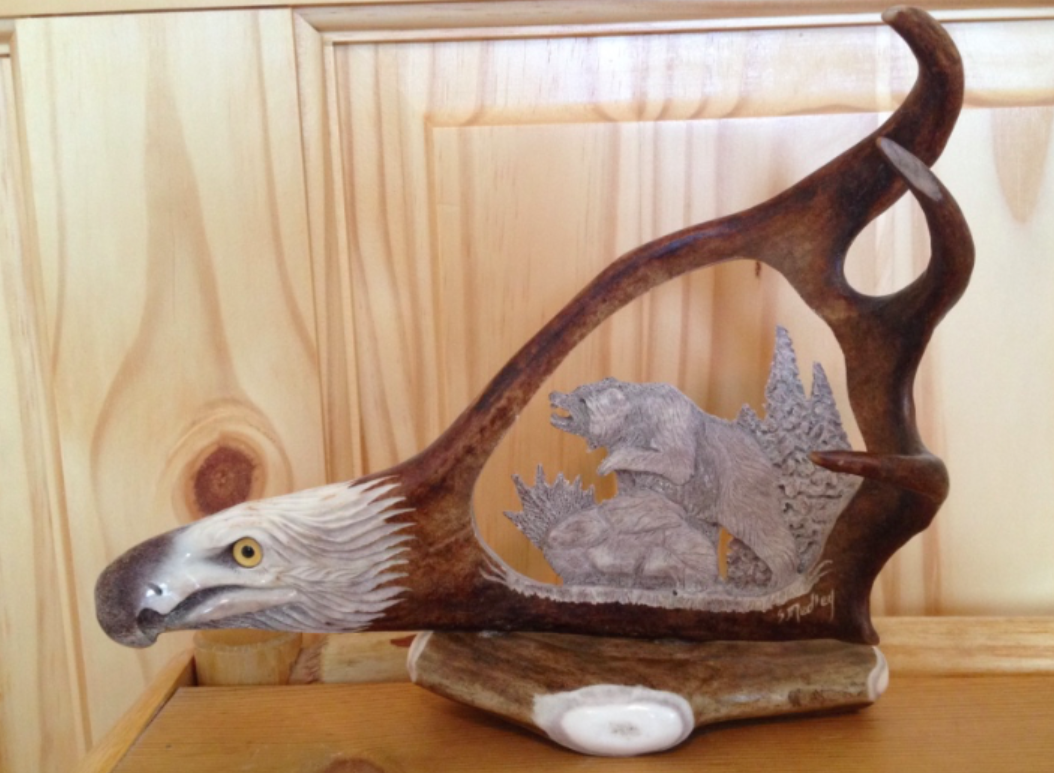 A handcrafted antler carving of a bear within the structure of a caribou antler, showcasing detailed artwork.